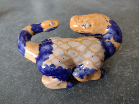 a ceramic figure of a quadrupedal creature with a long neck and snake head, and a smaller snake head at the end of its tail. the neck and tail are curved around so the heads are looking at each other.